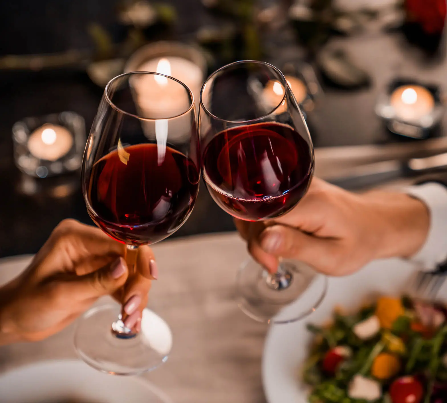 Close up of young couple toasting with glasses of red wine at restaurant