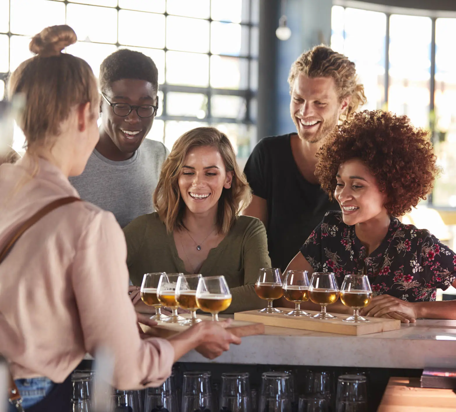 Waitress Serving Group Of Friends Beer Tasting In Bar